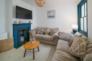 A living room with a blue fireplace, a sofa, a coffee table, and a television mounted on the wall. - Wistaria Cottage Beautifully Renovated Cottage (Cowes)