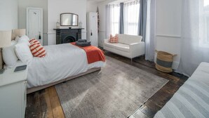 Ein Schlafzimmer mit Bett, Sofa, Kamin und einem Fenster mit Vorhängen.