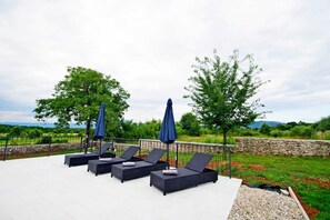 Eine Terrasse mit Liegestühlen und Sonnenschirmen, umgeben von Pflanzen und einer Steinmauer.