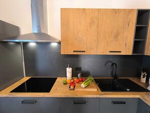 Eine Küche mit zwei schwarzen Induktionskochfeldern, einer Holz Arbeitsplatte und einem schwarzen Spülbecken.