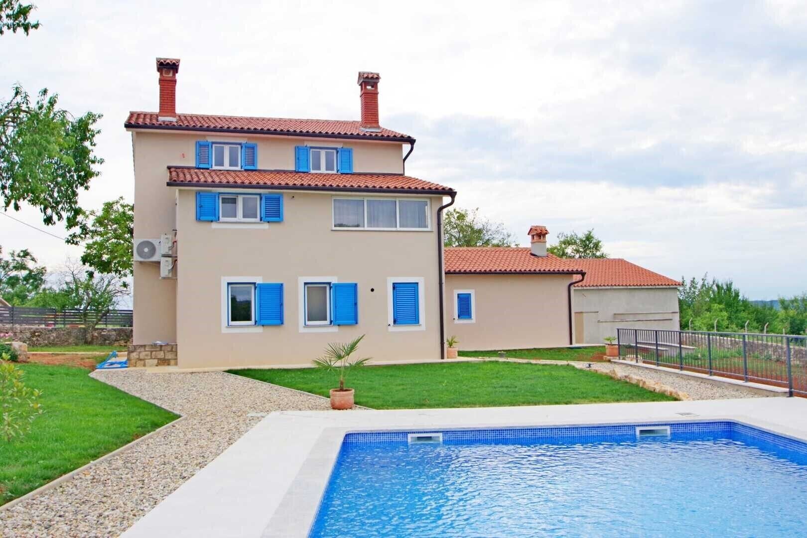 A two-story house with a swimming pool, a garden, and a clear sky.
