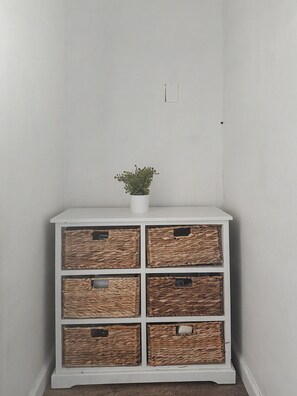 A white storage unit with six wicker baskets, each with a label, and a small potted plant on top.
