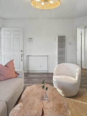 A living room with a white sofa, a white armchair, a wooden coffee table with a plant, a ceiling fan, and a white door. - Central Fremont. Convenient to all shops and downtown. Delux comfy. (Fremont)