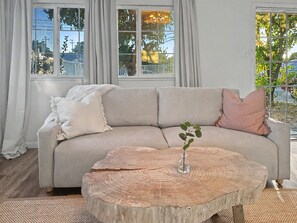 A living room with a sofa, a round coffee table with a tree stump top, and a vase with a plant.
