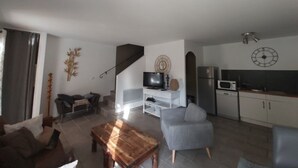 A modern living room with a sofa, a coffee table, a TV, and a kitchen area with a microwave and cabinets. - Charming country house with private pool (Nyons)