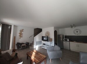 Ein modernes Wohnzimmer mit einer Couch, einem Couchtisch, einem Fernseher und einer Küchenzeile inklusive Mikrowelle und Schränken.