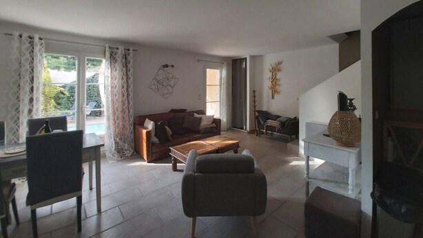 A spacious living room with a sofa, coffee table, and a fireplace. There is a dining area with a table and chairs, and a staircase leading to an upper level. - Charming country house with private pool (Nyons)