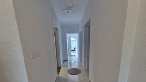 Un pasillo con paredes blancas, suelo de mármol y una puerta al final que da a una habitación.