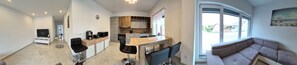 A modern living room with a sofa, a TV, and a kitchen area with a dining table and chairs.