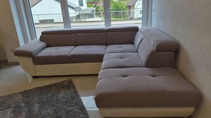 Un sofá modular en una habitación con ventanas amplias, una alfombra y vistas a casas.