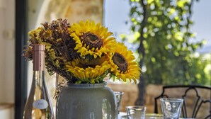 Ein Esstisch mit einer Vase voller Sonnenblumen, einer Weinflasche und leeren Gläsern.
