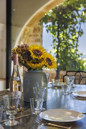 A dining table with a vase of sunflowers, a wine bottle, and empty glasses. - Villa Le Pré Neuf – Pool & Panoramic Views (Tourrettes-sur-Loup)