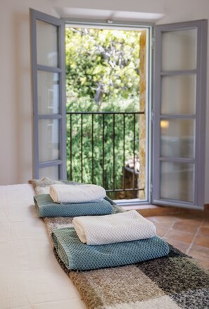 A room with a bed, a window with a view of greenery, and a balcony with a railing. - Villa Le Pré Neuf – Pool & Panoramic Views (Tourrettes-sur-Loup)