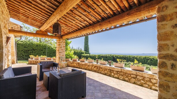 Eine überdachte Terrasse mit Korbmöbeln, Steinpfeilern und Topfpflanzen.