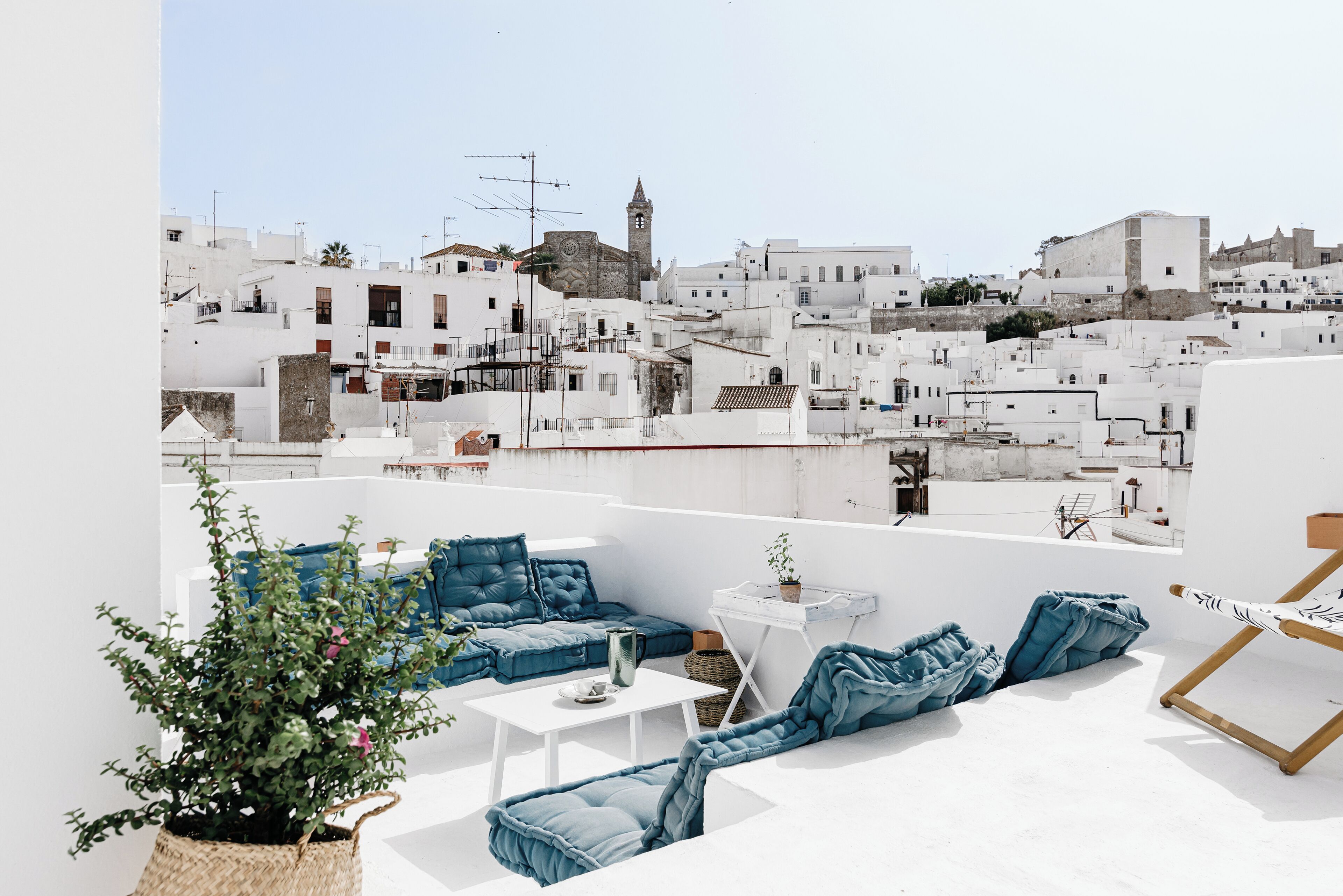 A rooftop terrace with white walls, a blue sofa set, a small table, and a potted plant.