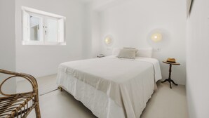 Un dormitorio con cama, ventana, ventilador de techo y una mesita con un sombrero.