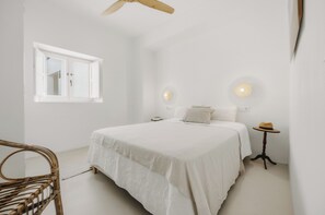 A bedroom with a bed, a window, a ceiling fan, and a small table with a hat. - Beautiful house in the historic center of Vejer de la Frontera (Vejer de la Frontera)