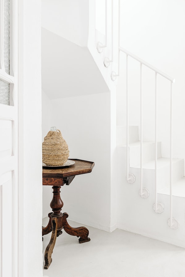 A white interior with a wooden table and a wicker basket, a white staircase, and a white railing. - Beautiful house in the historic center of Vejer de la Frontera (Vejer de la Frontera)
