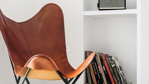 Una silla moderna de diseño único, una pared blanca y una estantería con libros y un altavoz.
