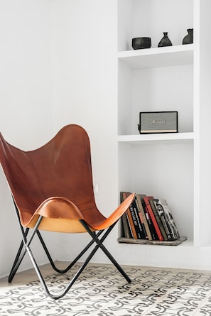 A modern chair with a unique design, a white wall, and a shelf with books and a speaker. - Beautiful house in the historic center of Vejer de la Frontera (Vejer de la Frontera)