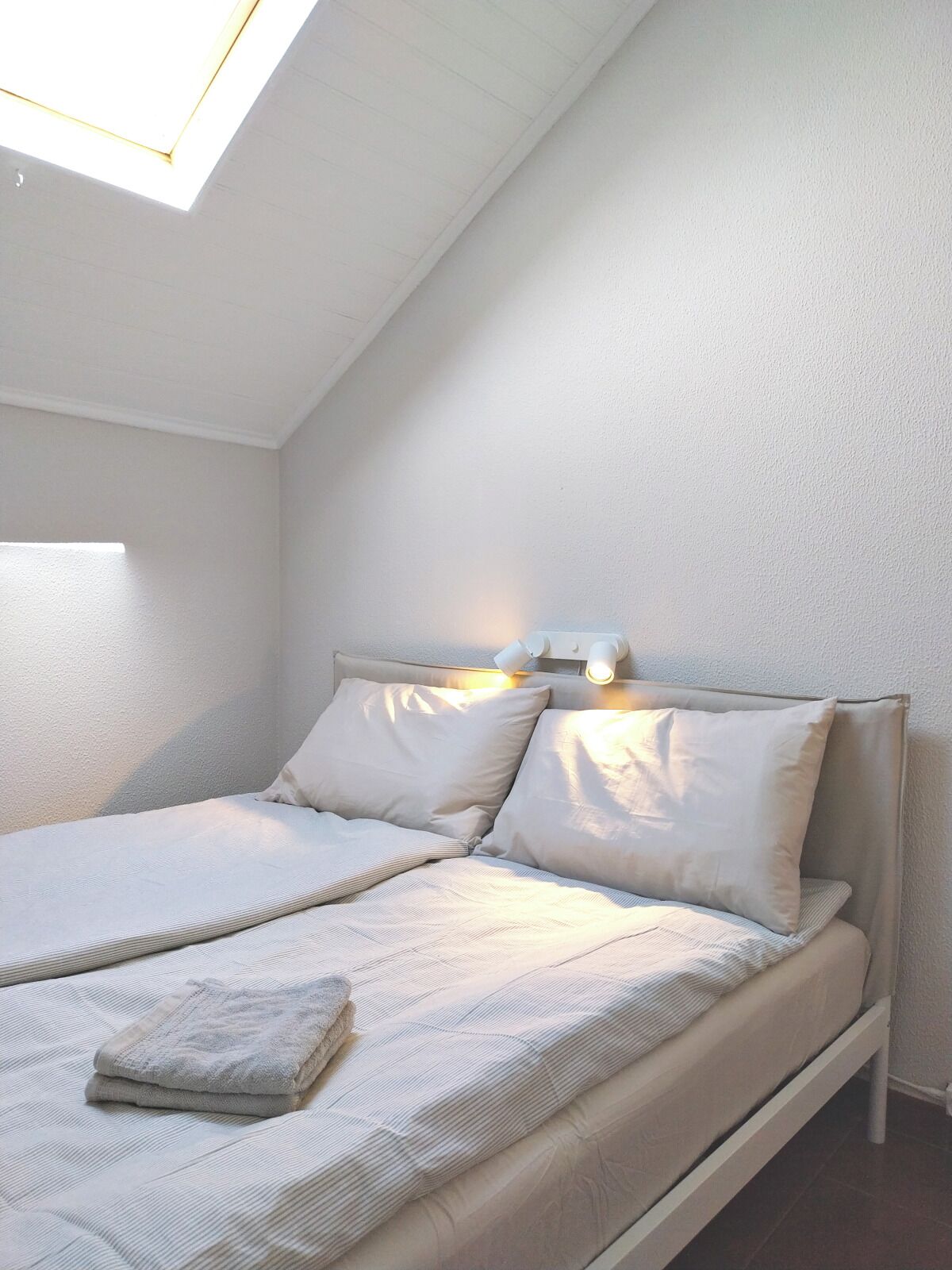 Ein Einzelbett mit Kopfteil, Nachttisch und Oberlicht.