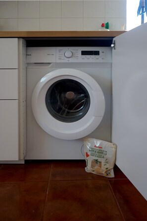 A front-loading washing machine in a kitchen with a tiled floor and a countertop above. - Old Town Apartment with Ocean Views (Sesimbra)