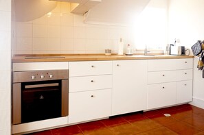 A kitchen with white cabinets, a stainless steel oven, a wooden countertop, and a window providing natural light. - Old Town Apartment with Ocean Views (Sesimbra)