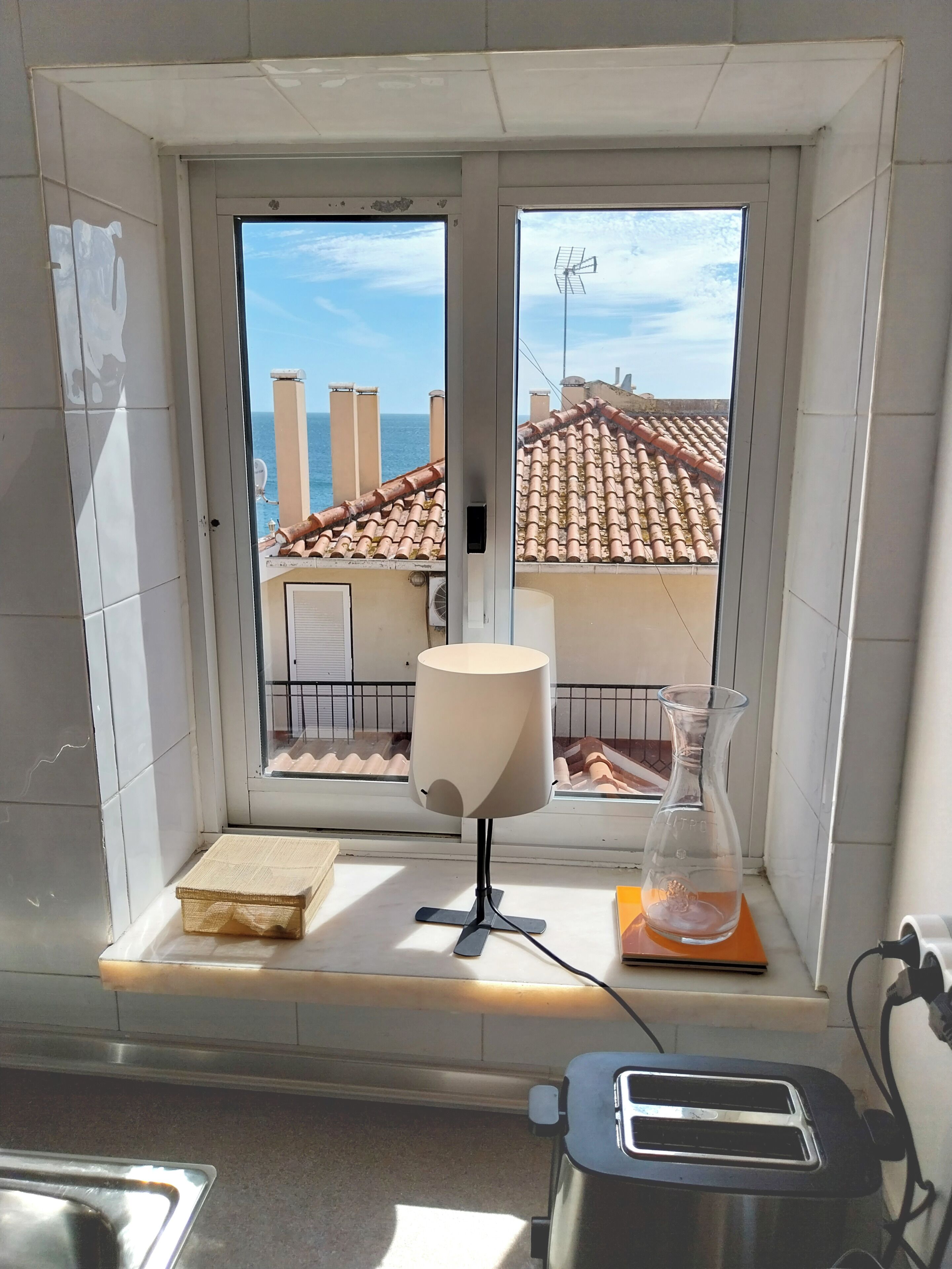 Une cuisine avec une fenêtre, un grille-pain, une lampe et un vase.