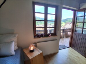 A room with a bed, a nightstand with a lamp, a window with a view of the outdoors, and a radiator. - Höflepanorama Apartment: Sauna, Fireplace, Grill, View, Balcony, Groups, Wi-Fi (Oppenau)