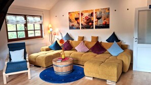 A living room with a sofa, a chair, a wooden barrel, and a vase with flowers. - Höflepanorama Apartment: Sauna, Fireplace, Grill, View, Balcony, Groups, Wi-Fi (Oppenau)