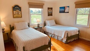 A bedroom with two beds, a small table with a lamp, and a window with a view of a grassy area. - Walk to the beach! Entire home in Nantucket, Massachusetts (Nantucket)