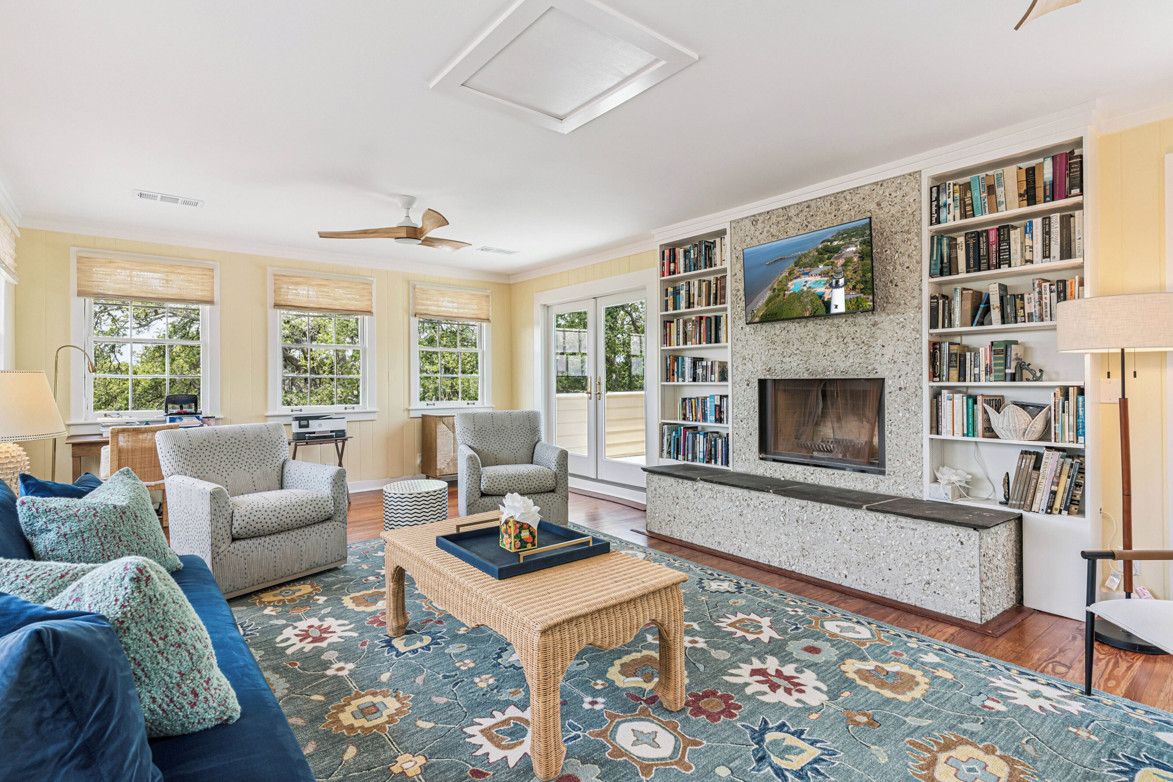 A spacious living room with a fireplace, a bookshelf, and a large window.
