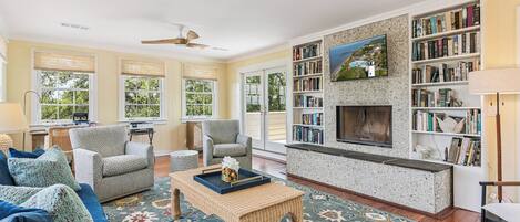 A spacious living room with a fireplace, a bookshelf, and a large window.