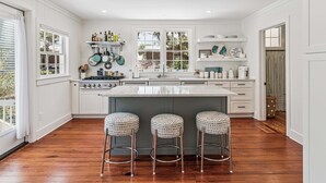 Une cuisine avec des meubles blancs, un îlot central et trois tabourets.