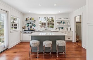 A kitchen with white cabinets, a central island, and three stools. - Upscale East Beach & Pool (St Simons Island)