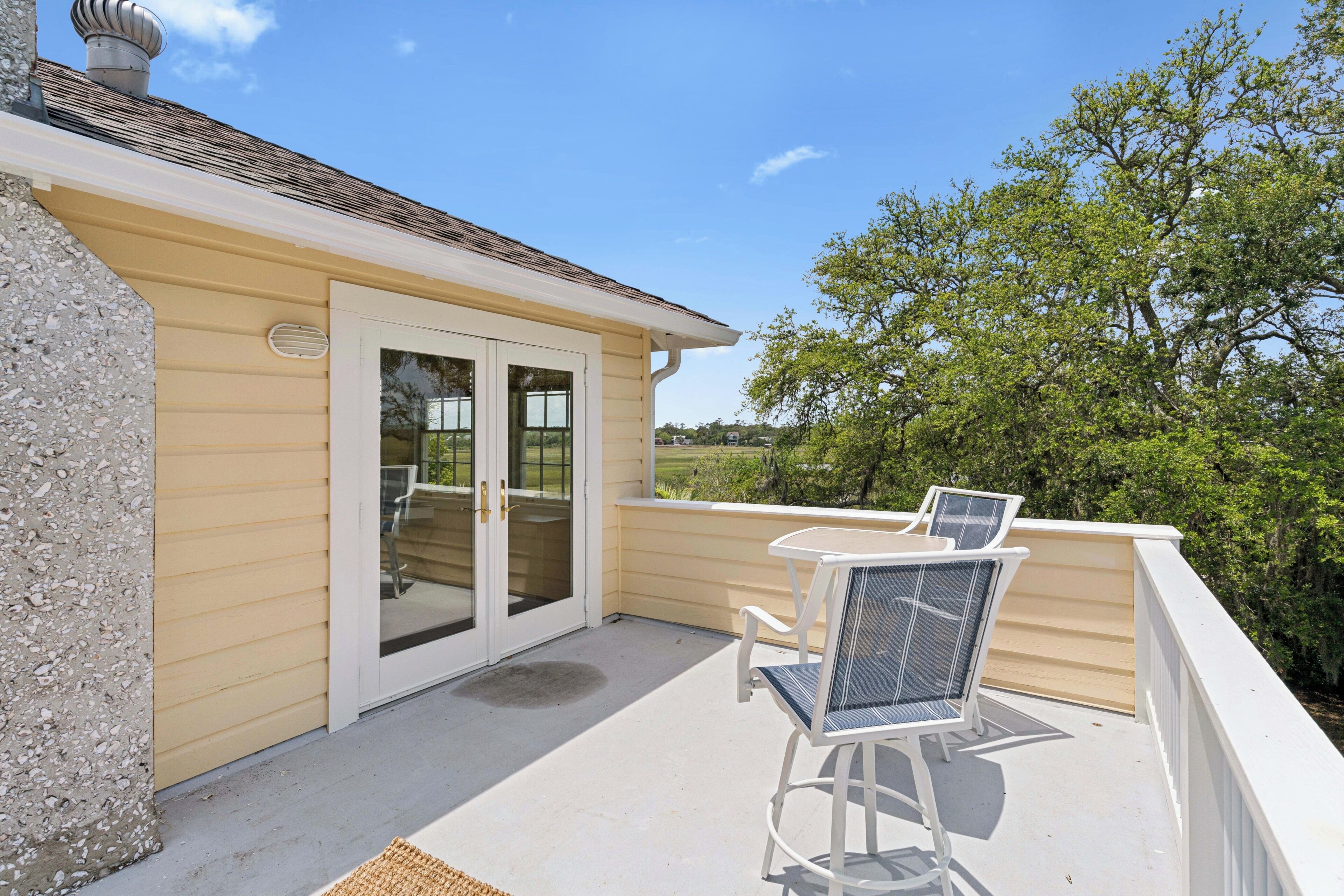 A covered patio with two chairs and a table, a sliding glass door, and a view of trees.