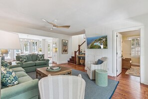 A spacious living room with a green sofa set, a wooden coffee table, and a television mounted on the wall. - Upscale East Beach & Pool (St Simons Island)