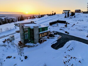 A modern building with a glass facade, situated on a snow-covered slope with a clear view of the sunset in the background. - Ski in/ski out whole house rental-Powder Mountain, views, hot tub, sauna & more! (Eden)