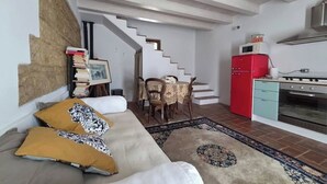 A living room with a sofa, a dining table with chairs, a staircase, a red refrigerator, and a stove. - Rider's lease in ancient Marche farmhouse amidst the hills (Marche)