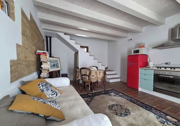 A living room with a sofa, a dining table with chairs, a staircase, a red refrigerator, and a stove. - Rider's lease in ancient Marche farmhouse amidst the hills (Marche)