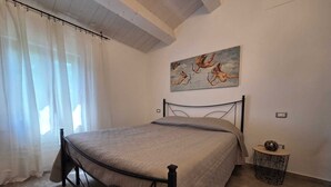 A bedroom with a bed, a painting, a small round table, and a curtain. - Rider's lease in ancient Marche farmhouse amidst the hills (Marche)
