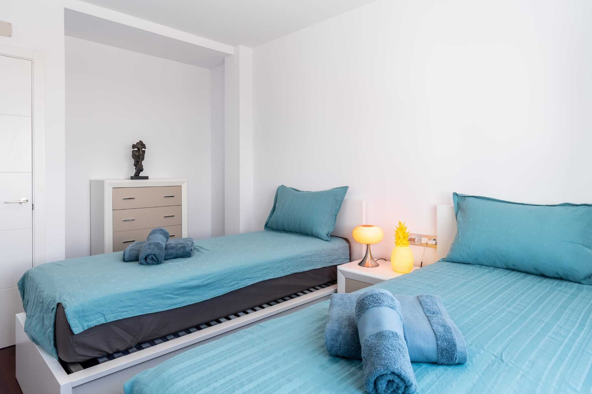 A bedroom with two beds, a nightstand with a lamp, and a small cabinet.