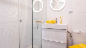 Ein modernes Badezimmer mit einer Duschkabine aus Glas, einem weißen Waschbecken mit einem gelben Handtuch und zwei runden Spiegeln.