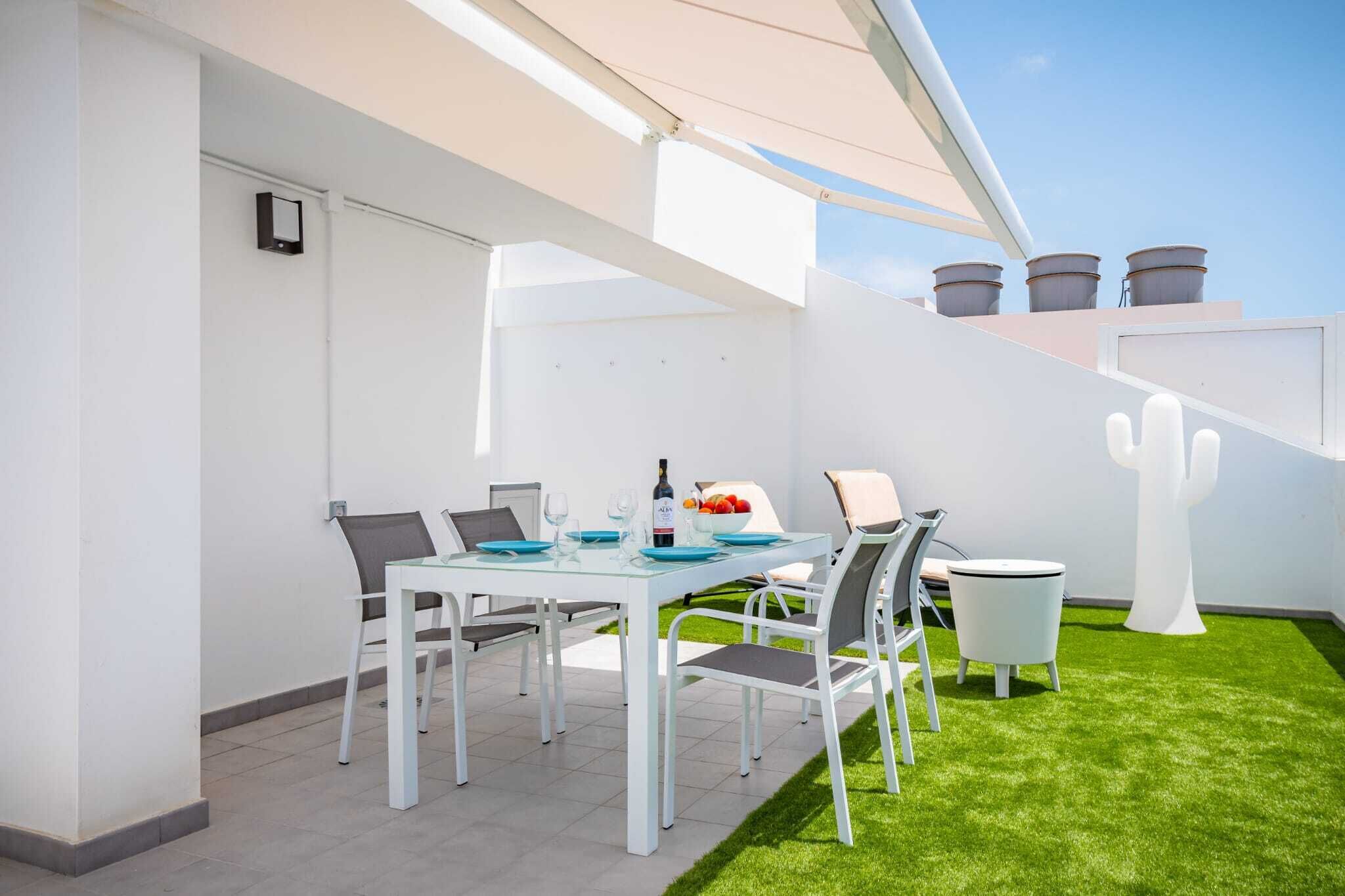 Un espacio exterior moderno con comedor, una mesa blanca y sillas, una mesa redonda pequeña y una escultura blanca.