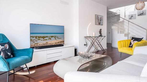 Ein modernes Wohnzimmer mit Flachbildfernseher, Glastisch und einer Treppe, die in eine obere Etage führt.