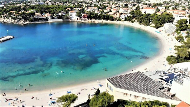 Un borgo costiero con una baia cristallina, spiaggia sabbiosa e un mix di edifici residenziali e commerciali.