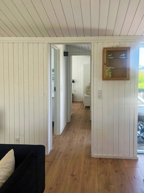 Ein Zimmer mit Holzböden, weißen Wänden, einem schwarzen Sofa, einem Holzschrank und einer Tür zu einem anderen Raum.