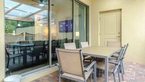 A patio area with a table and chairs, a sliding glass door, and a door to the right. - 5BR Solterra Home with Private Pool Near Disney (Davenport)