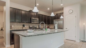 A kitchen with dark cabinets, a granite countertop, a microwave, a refrigerator, and pendant lighting. - 5BR Solterra Home with Private Pool Near Disney (Davenport)