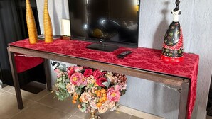 Een woonkamer met een televisie, een rode tafel en een bloemenboeket.